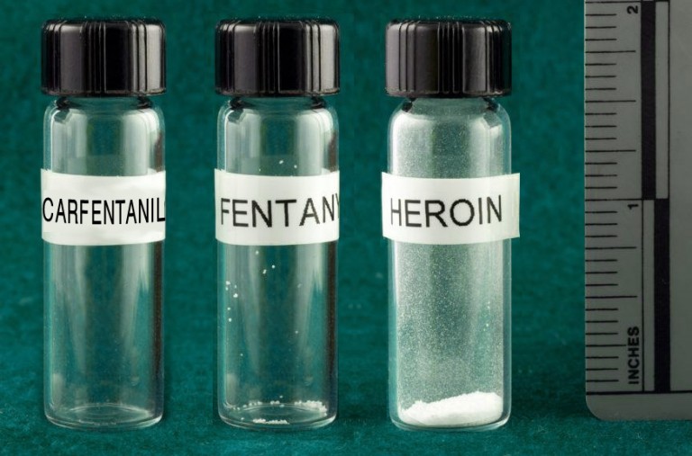 Drie gelabelde flesjes naast een liniaal met dodelijke doses carfentanil, fentanyl en heroïne, de eerste twee nauwelijks zichtbaar