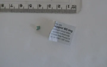 Fragment van een oxycodontablet naast het etiket van Oxypro 80 mg met verlengde afgifte